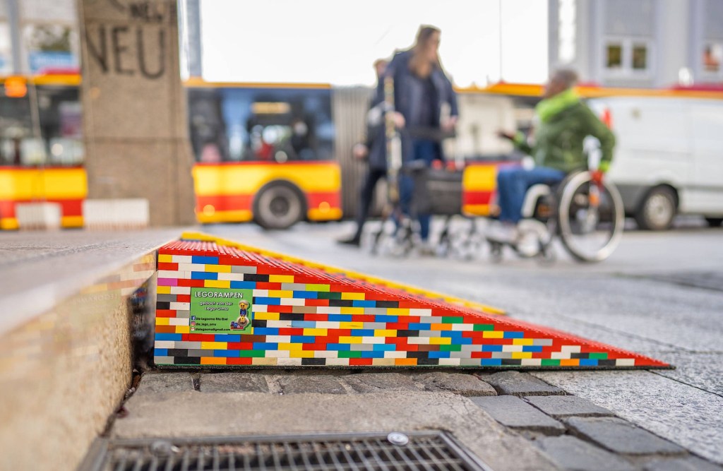 On the picture is a ramp build out of lego prics, and blurred in the background one can recognize a person in a wheelchair. 